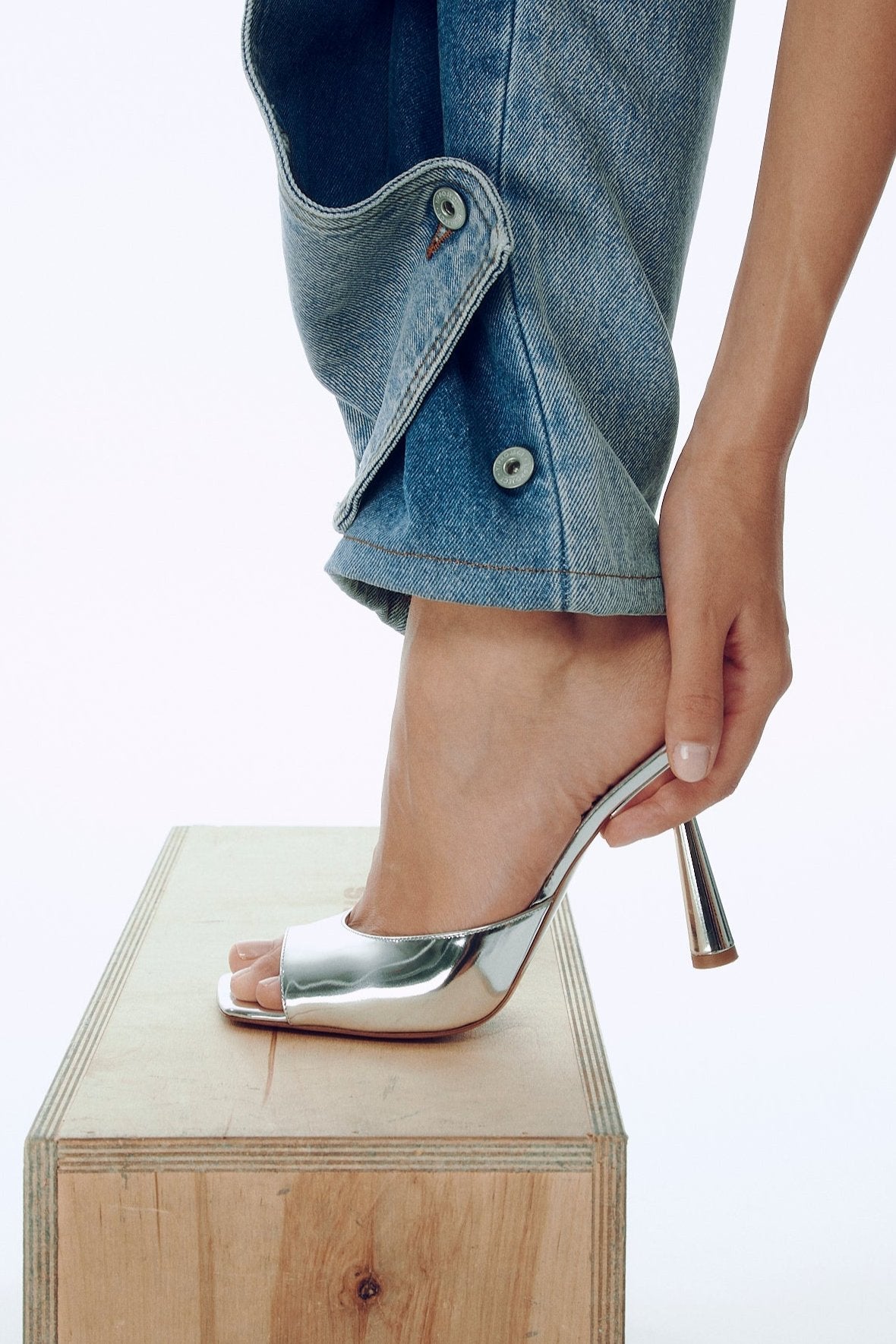 Silver high-heeled shoe being worn on a wooden block with a light background