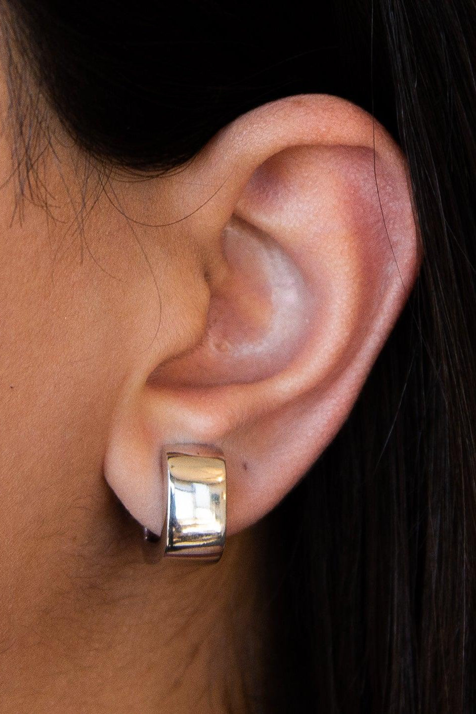 Silver squared hoop earring worn by a person with dark hair.