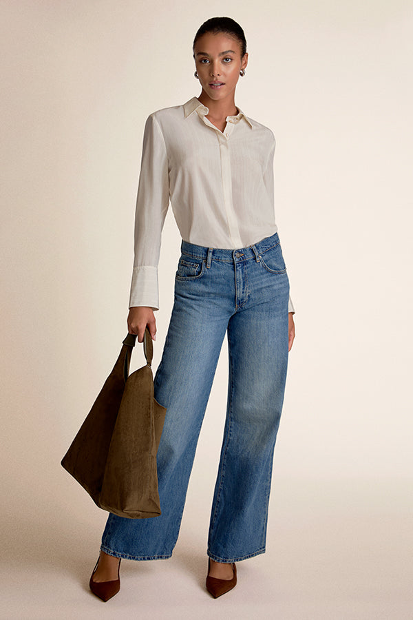 Woman wearing a white shirt and blue jeans holding a brown bag on a beige background | Exclude