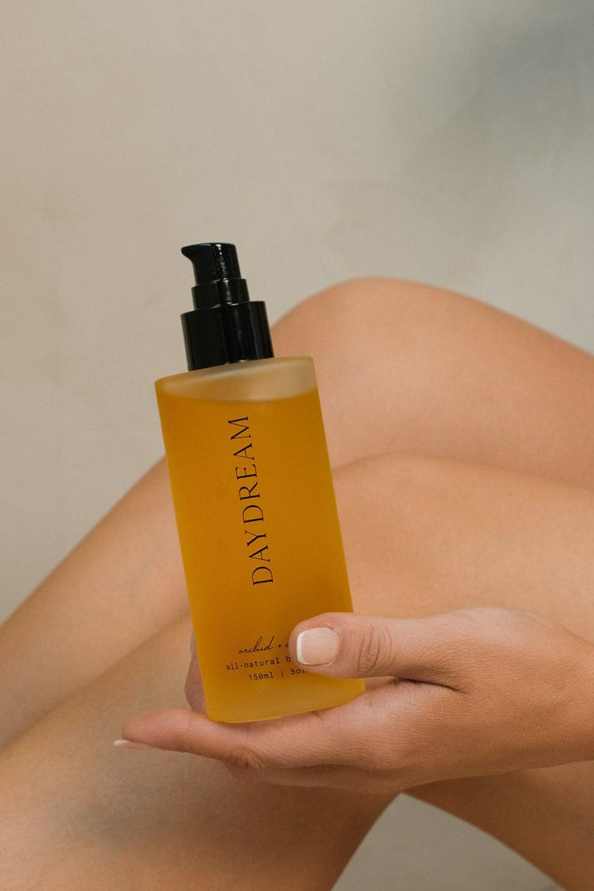 Hand holding a bottle of 'Daydream' product against a neutral background