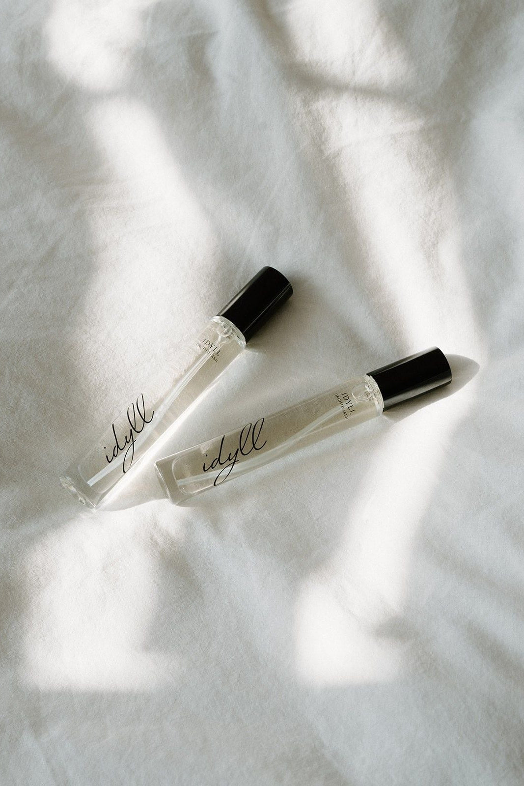 Two small bottles of 'Widely' on a textured white surface with soft shadows.