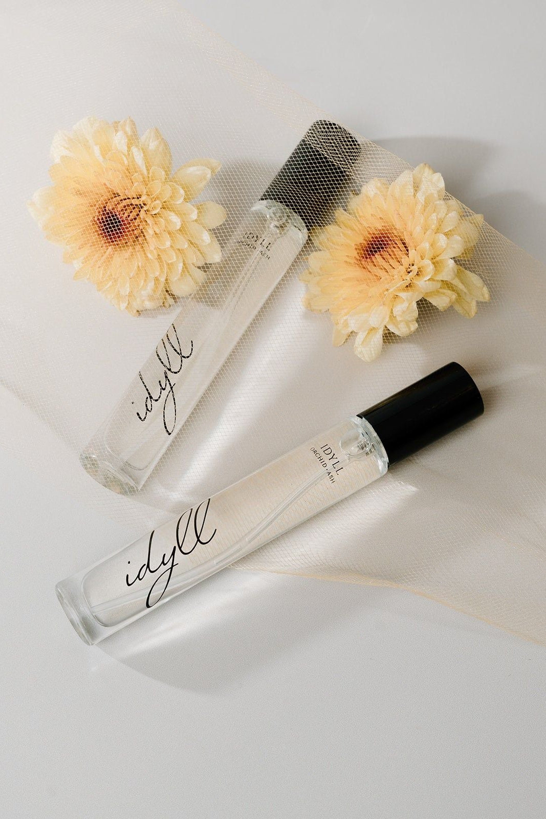 Two 'idyll' perfume bottles with flowers on a light background