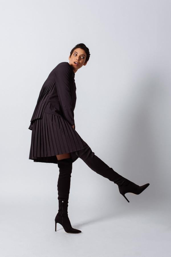 Person wearing a black outfit with a skirt and knee-high boots on a white background