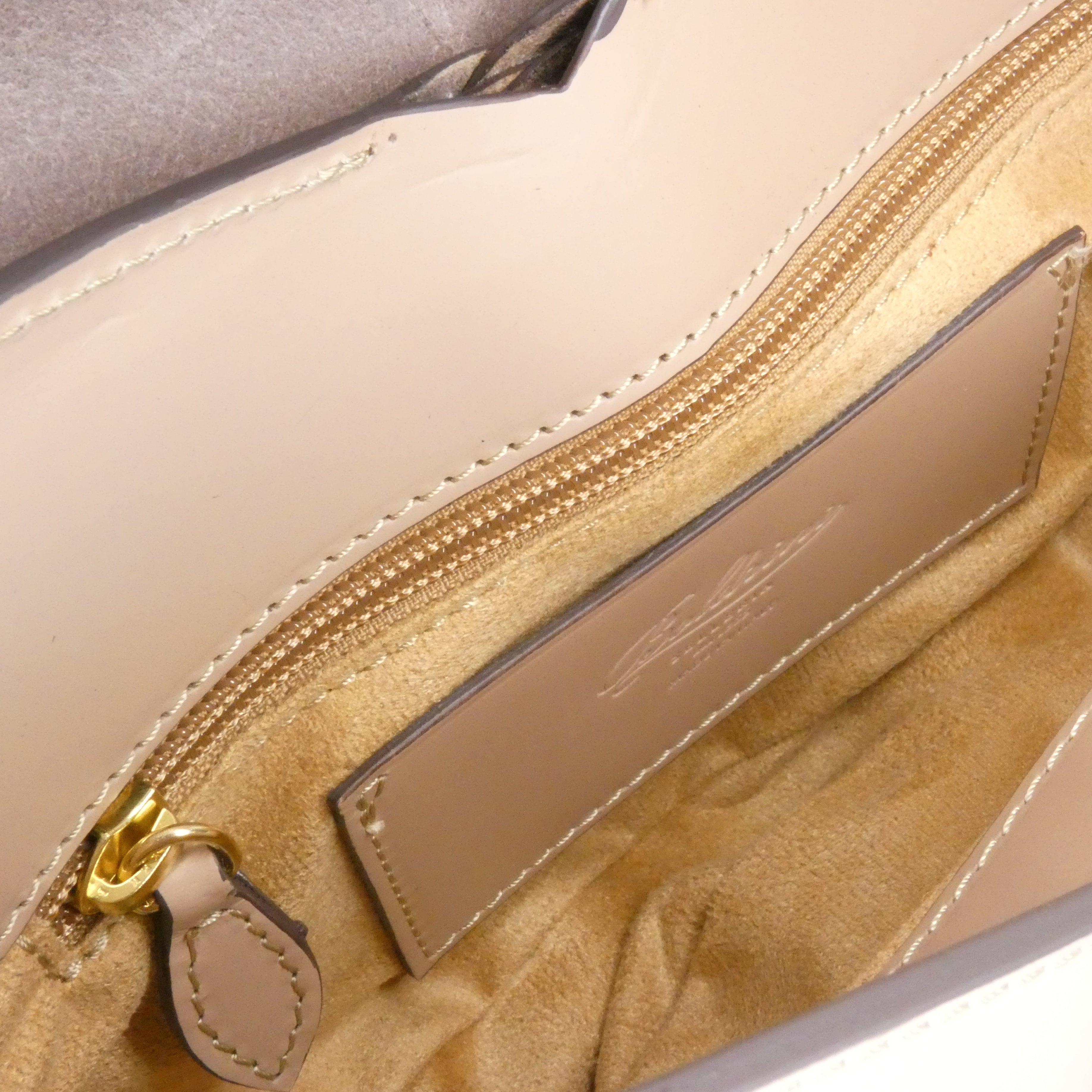 Close-up of a beige handbag with a gold zipper and visible brand label.