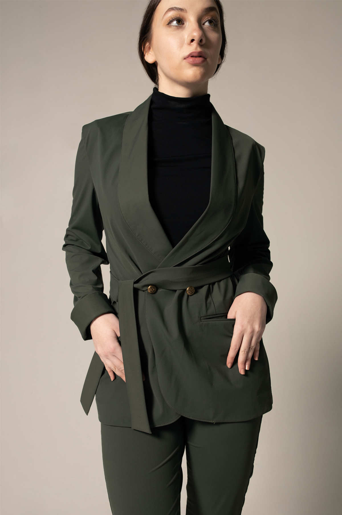 Woman wearing a green blazer and black turtleneck against a beige background