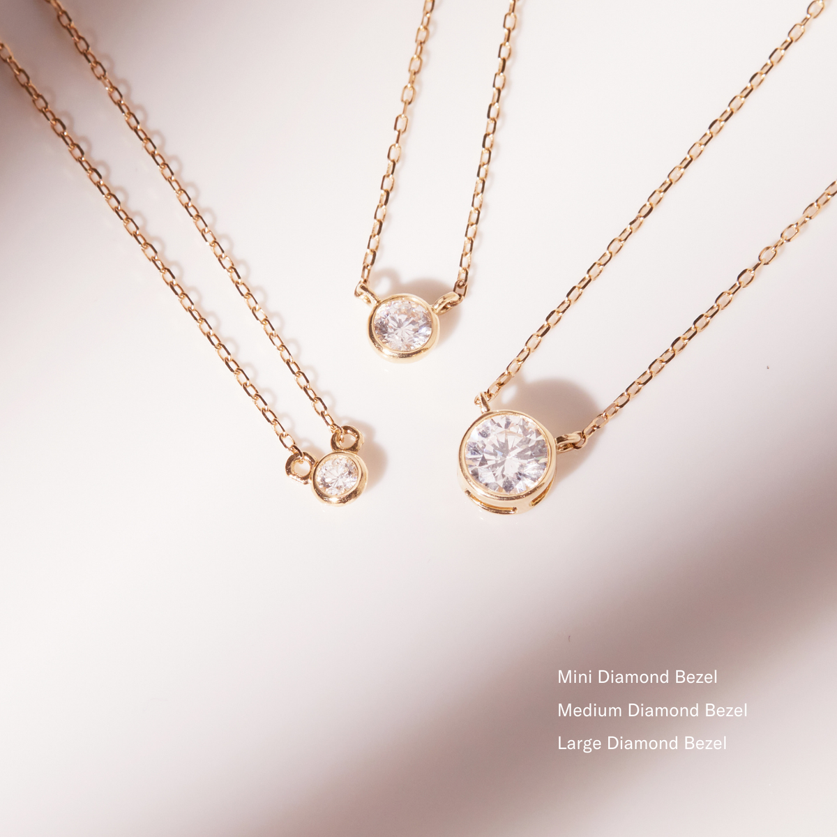 Three gold necklaces with diamond bezels on a light pink background