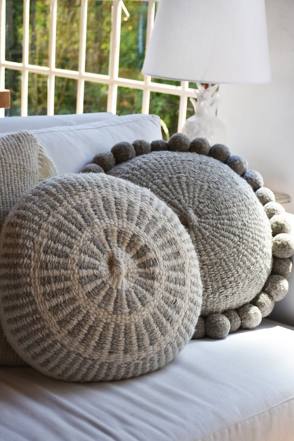Round textured pillows with pom-pom details on a white surface.