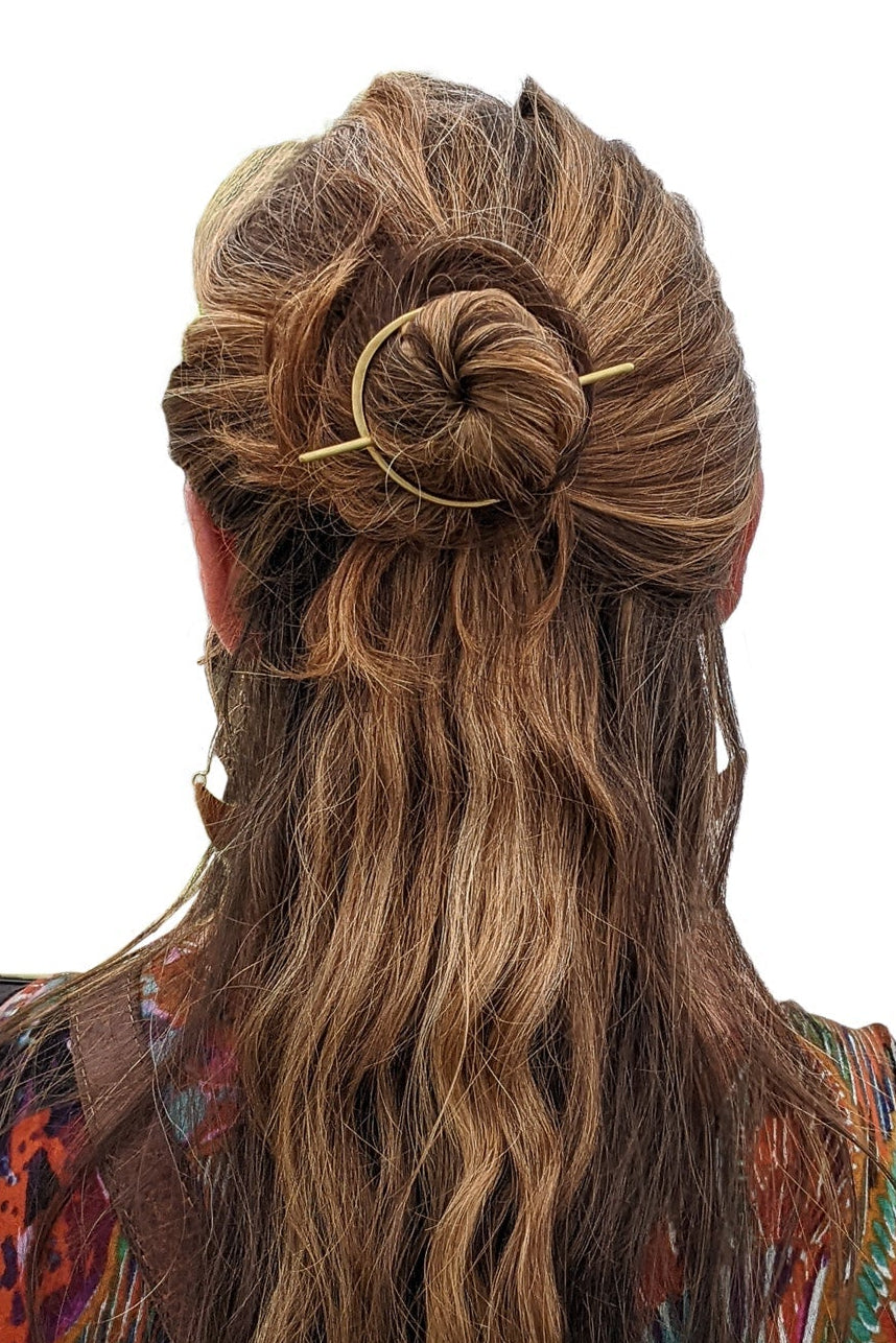 Woman with long, wavy hair styled in a bun with a decorative hairpin on a white background