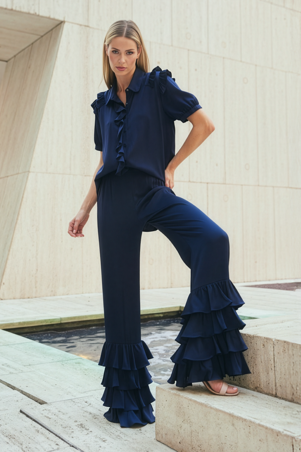 Woman wearing a navy blue ruffled silk outfit standing on steps with a modern architectural background.