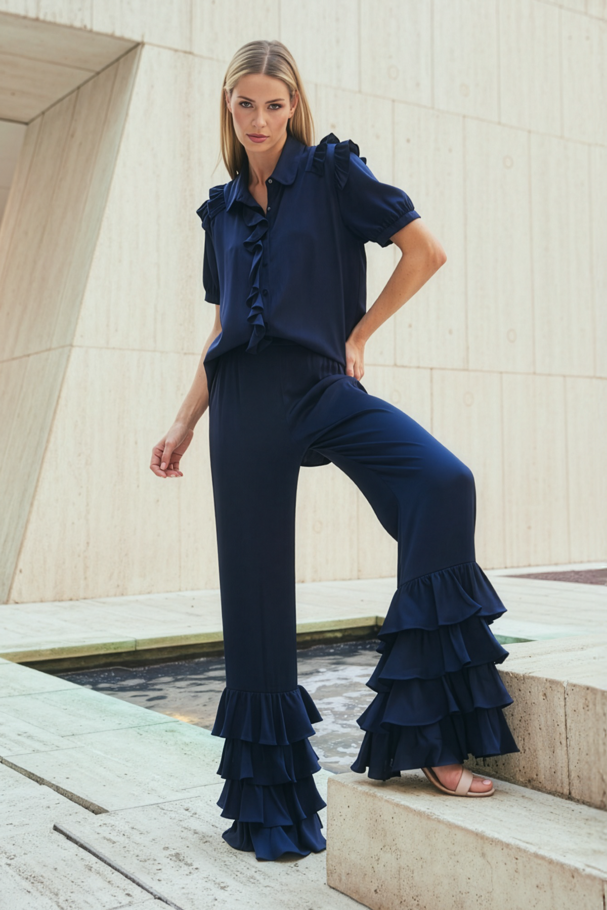 Woman wearing a navy blue ruffled outfit standing on steps with a modern architectural background.