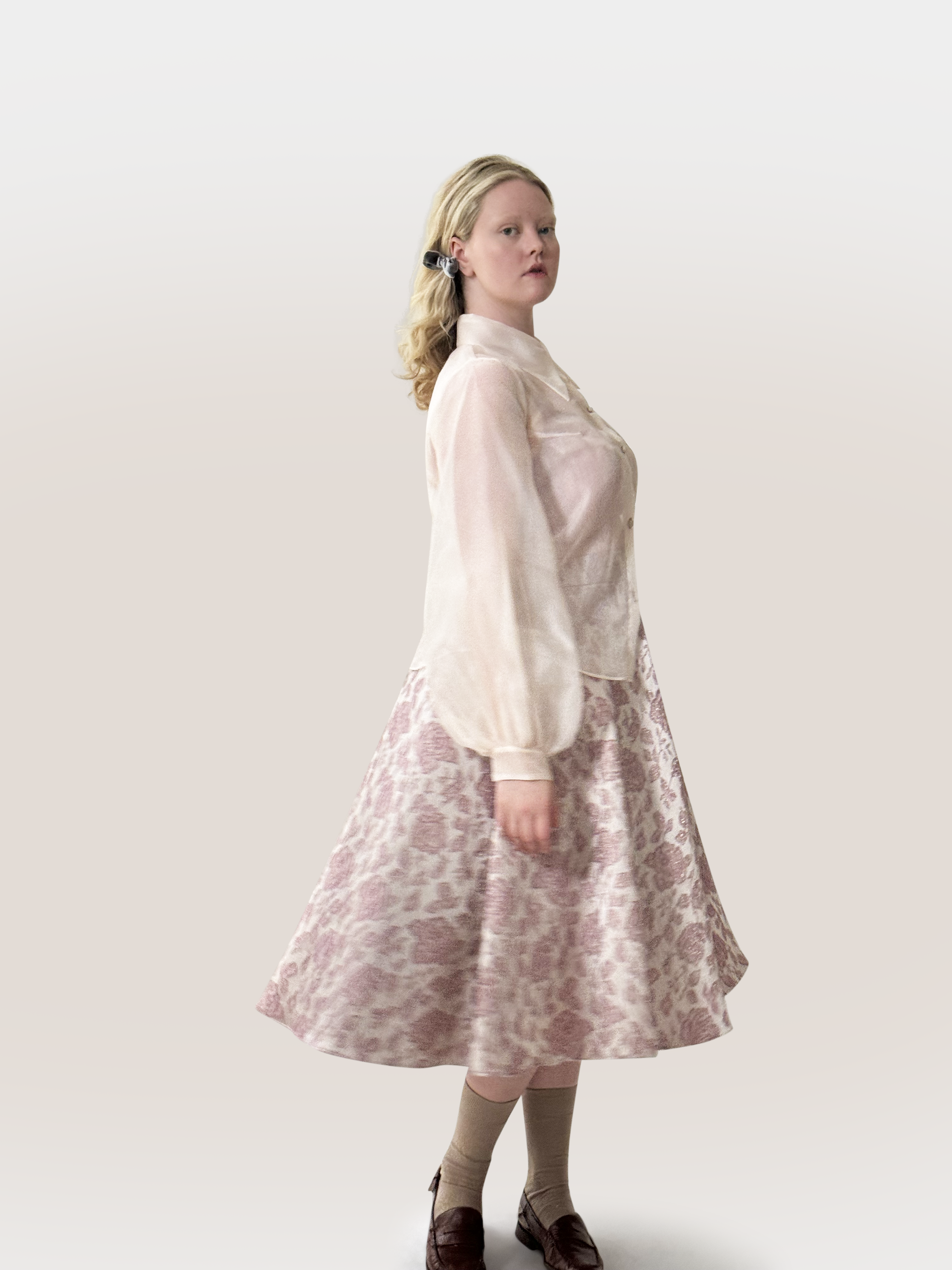 Woman wearing a light pink blouse and floral skirt against a white background