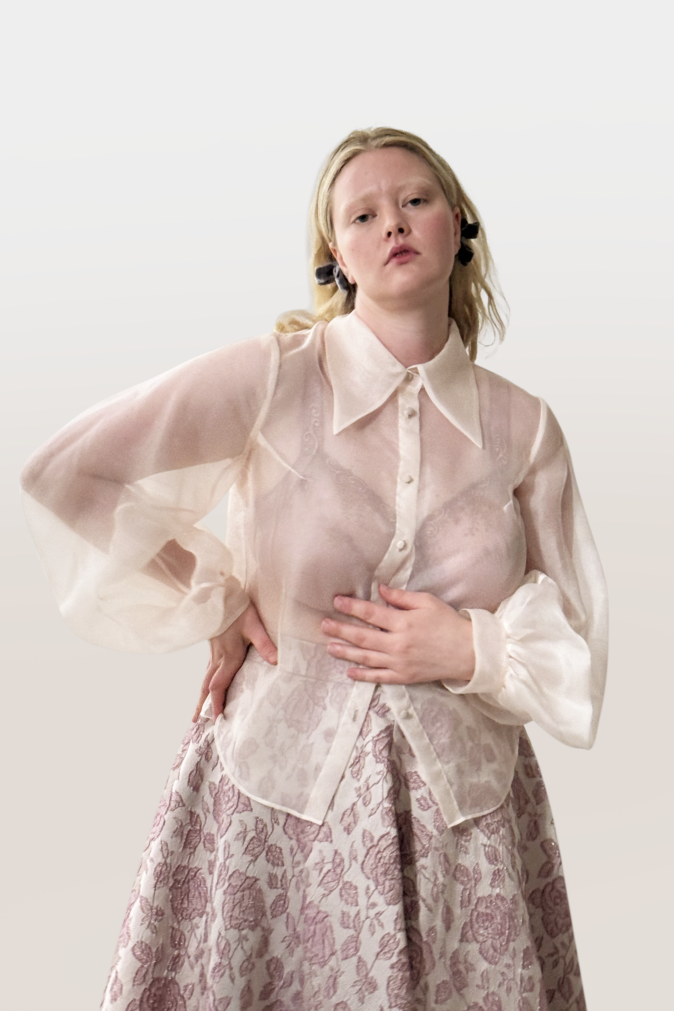 Woman wearing a sheer white blouse over a patterned skirt on a plain background