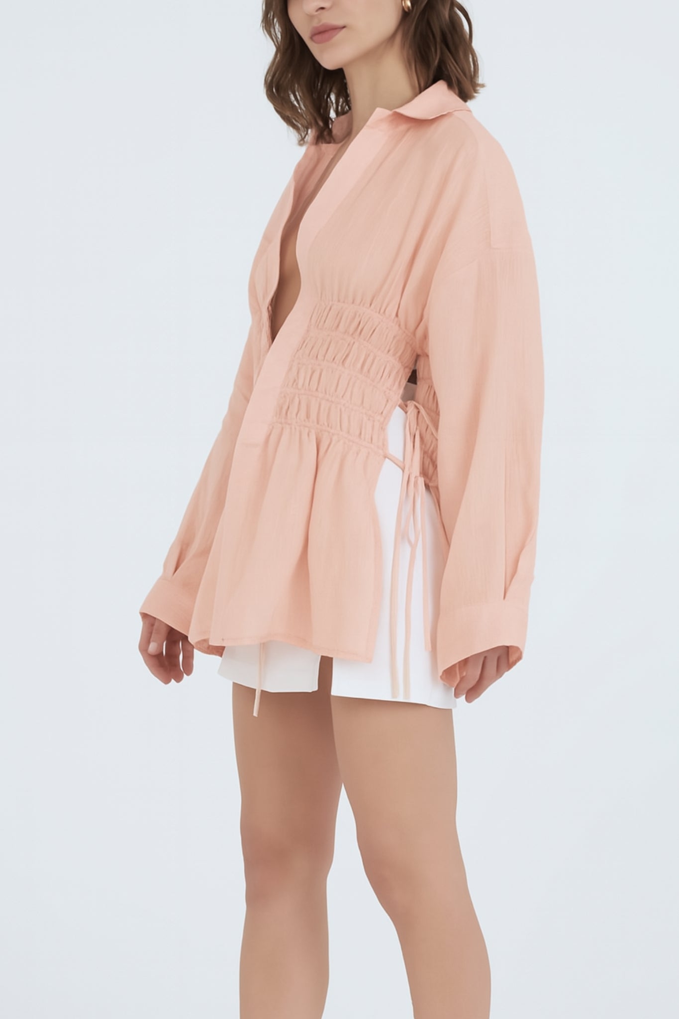 Woman wearing a peach-colored blouse with long sleeves on a light gray background