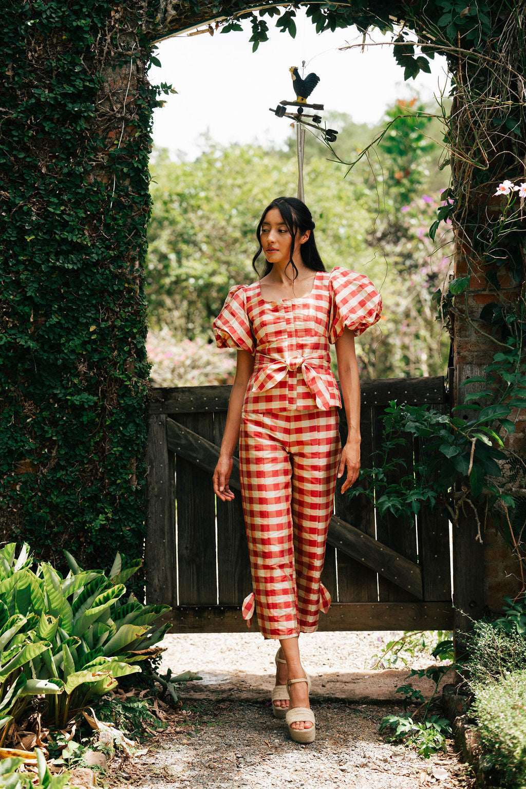 Woman in a red and white checkered outfit standing in a garden.