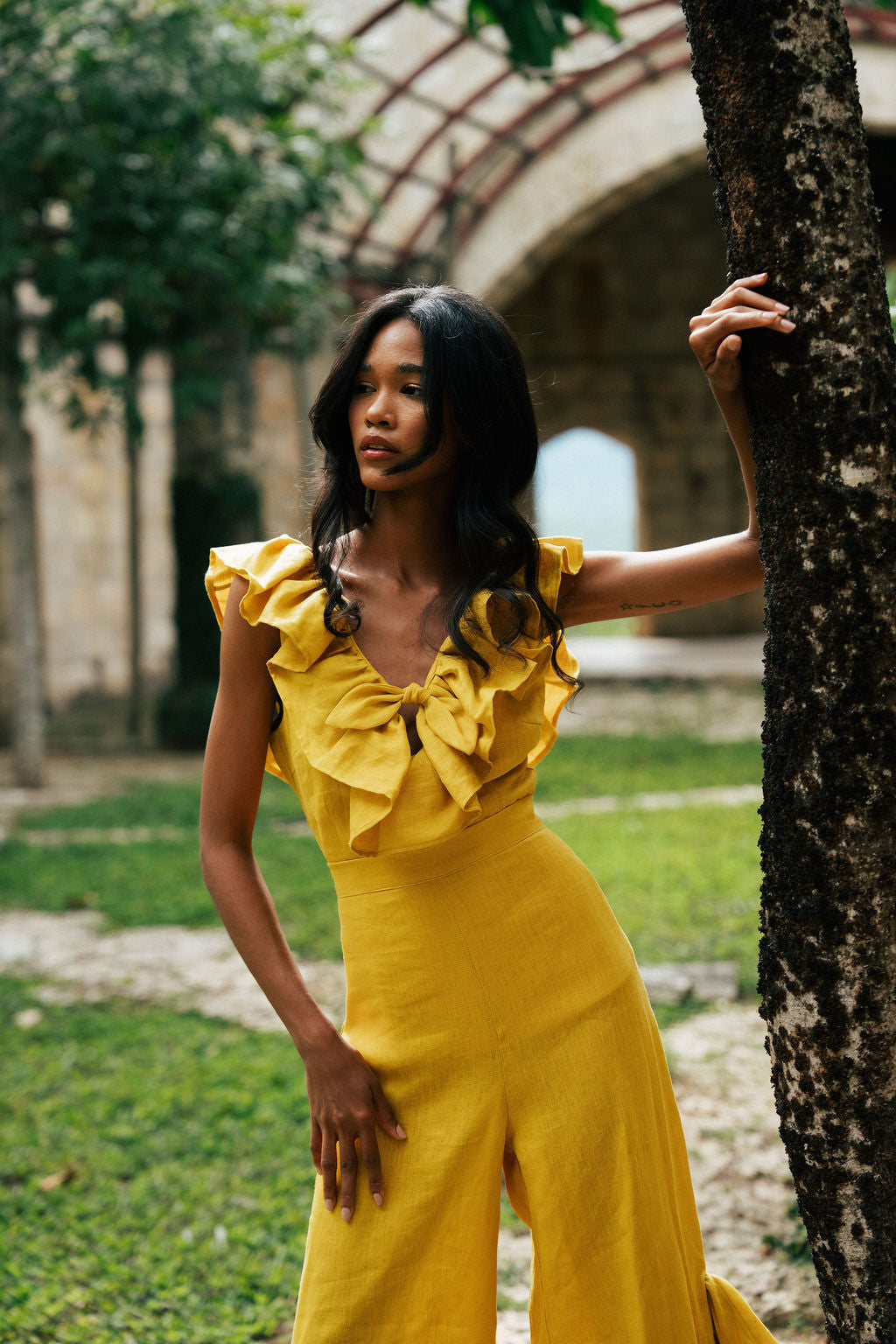 Woman in a yellow dress standing next to a tree in an outdoor setting