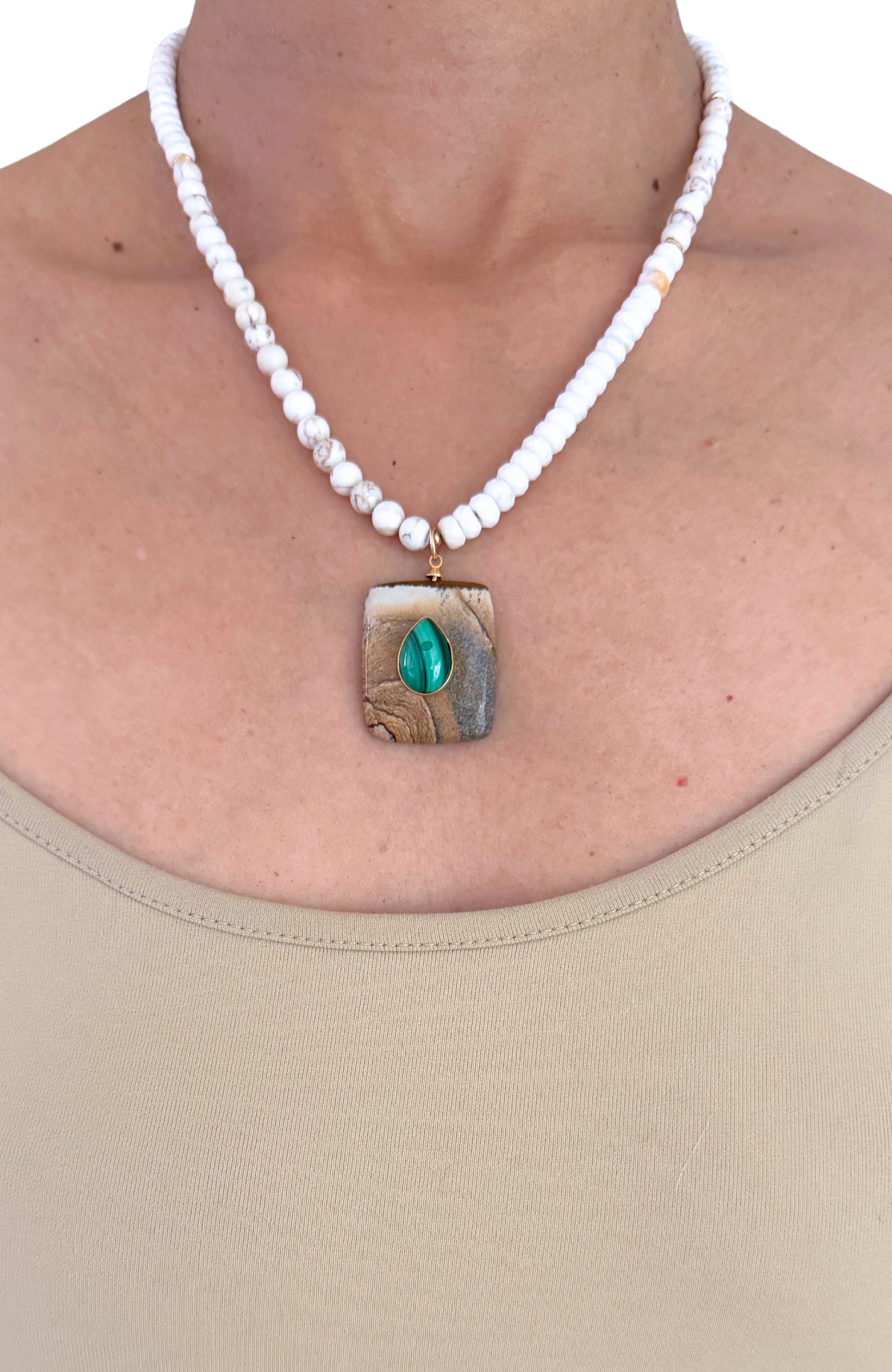 Necklace with a square pendant featuring a green stone worn by a person.