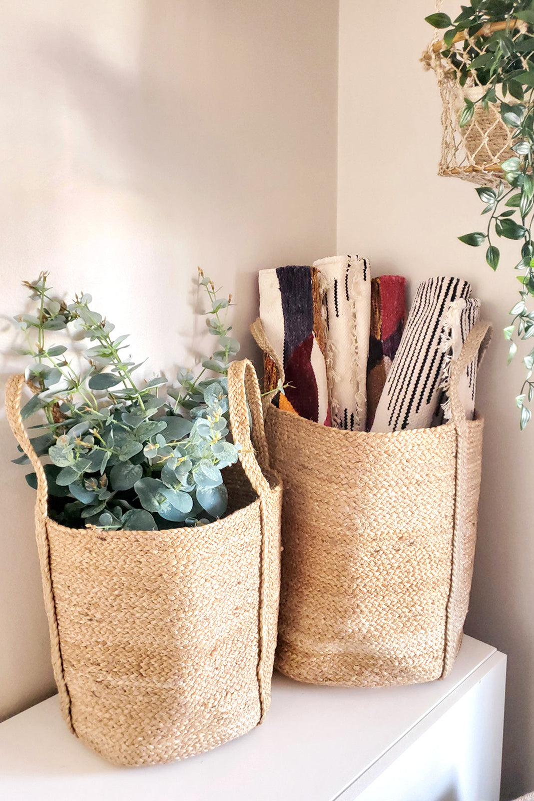 Two woven baskets on a white surface with plants and books inside.