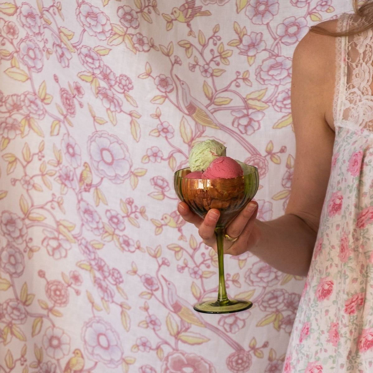 Person holding a glass with two scoops of ice cream against a floral patterned background