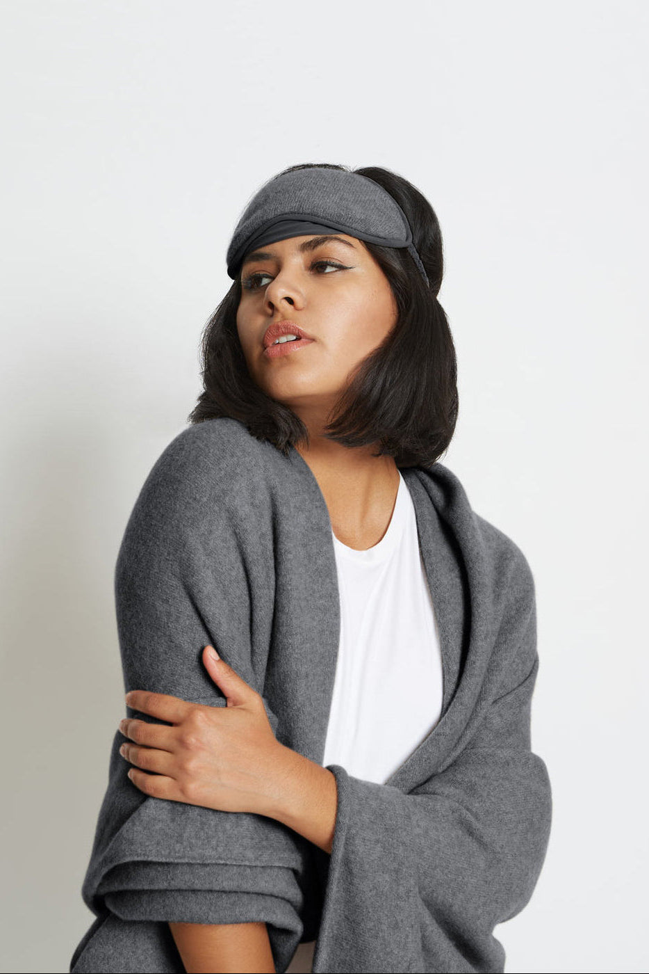 Woman wearing a gray cardigan and cap against a white background