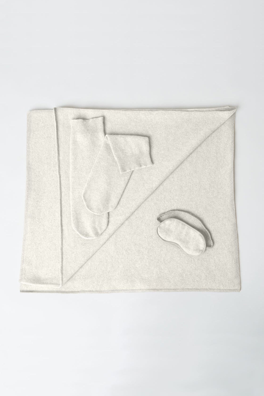 Set of white bath items including a towel, washcloth, and eye mask on a light gray background