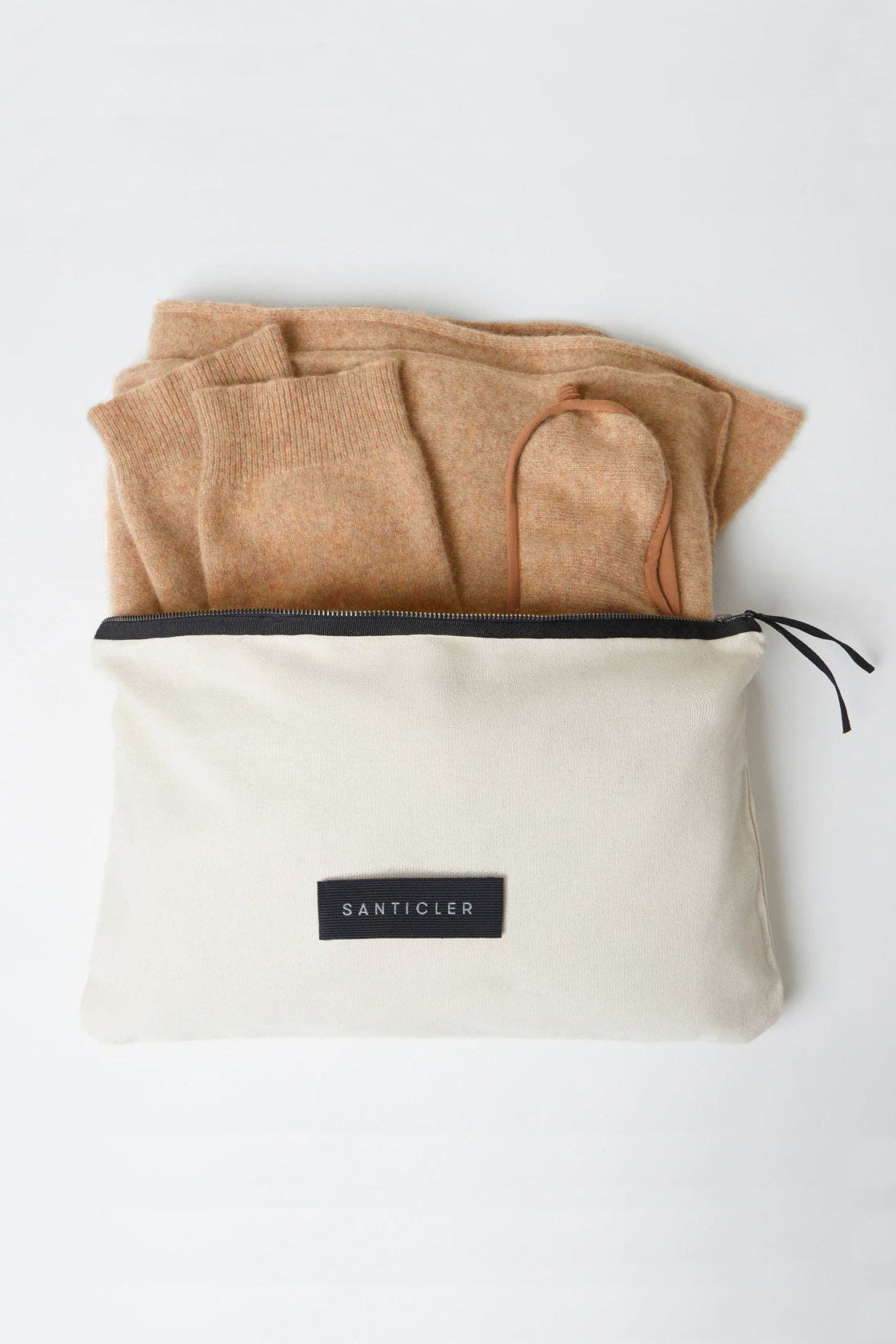 Beige folded fabric and a beige pouch with a black label on a white background