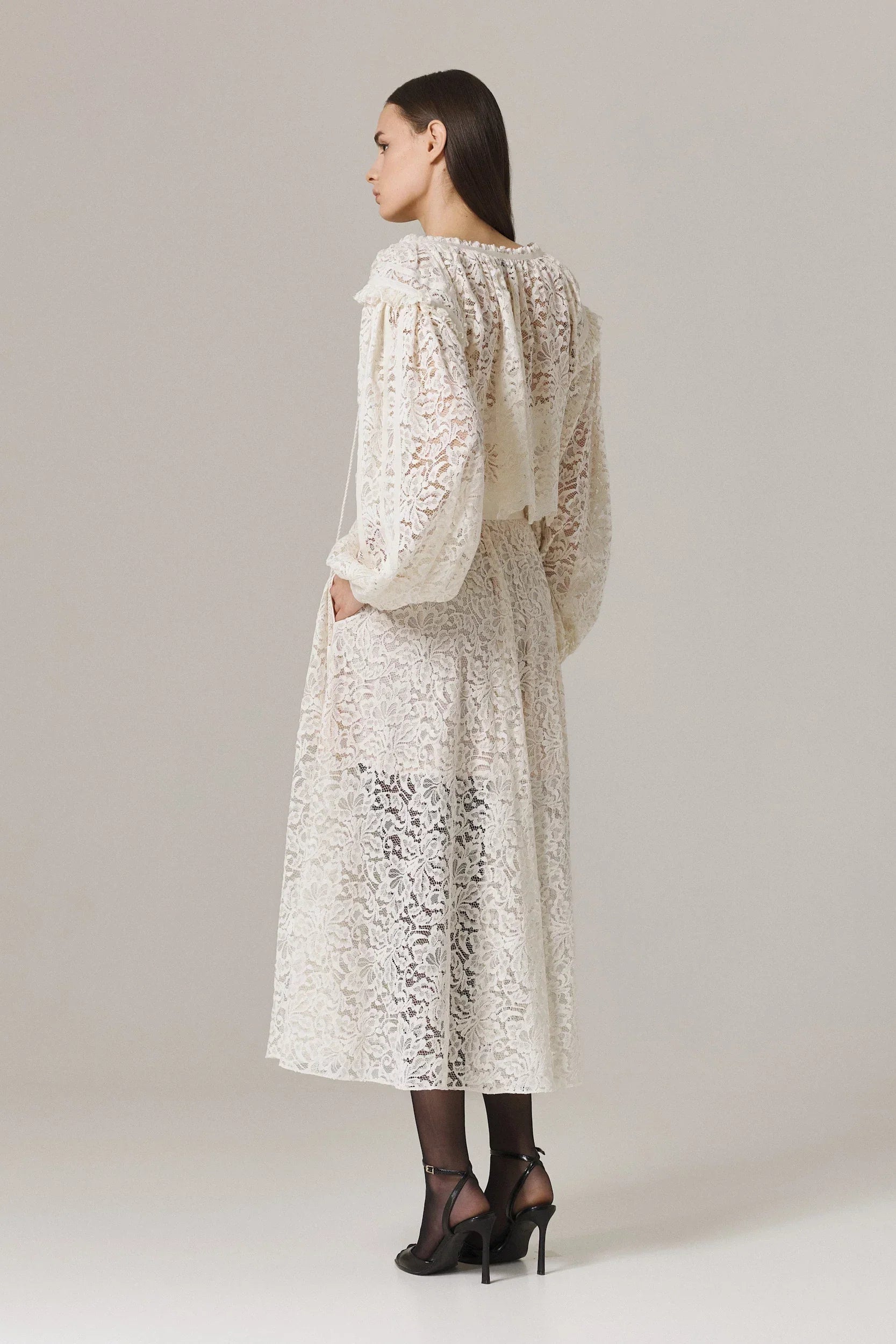 Woman wearing a long, light-colored lace dress against a plain background