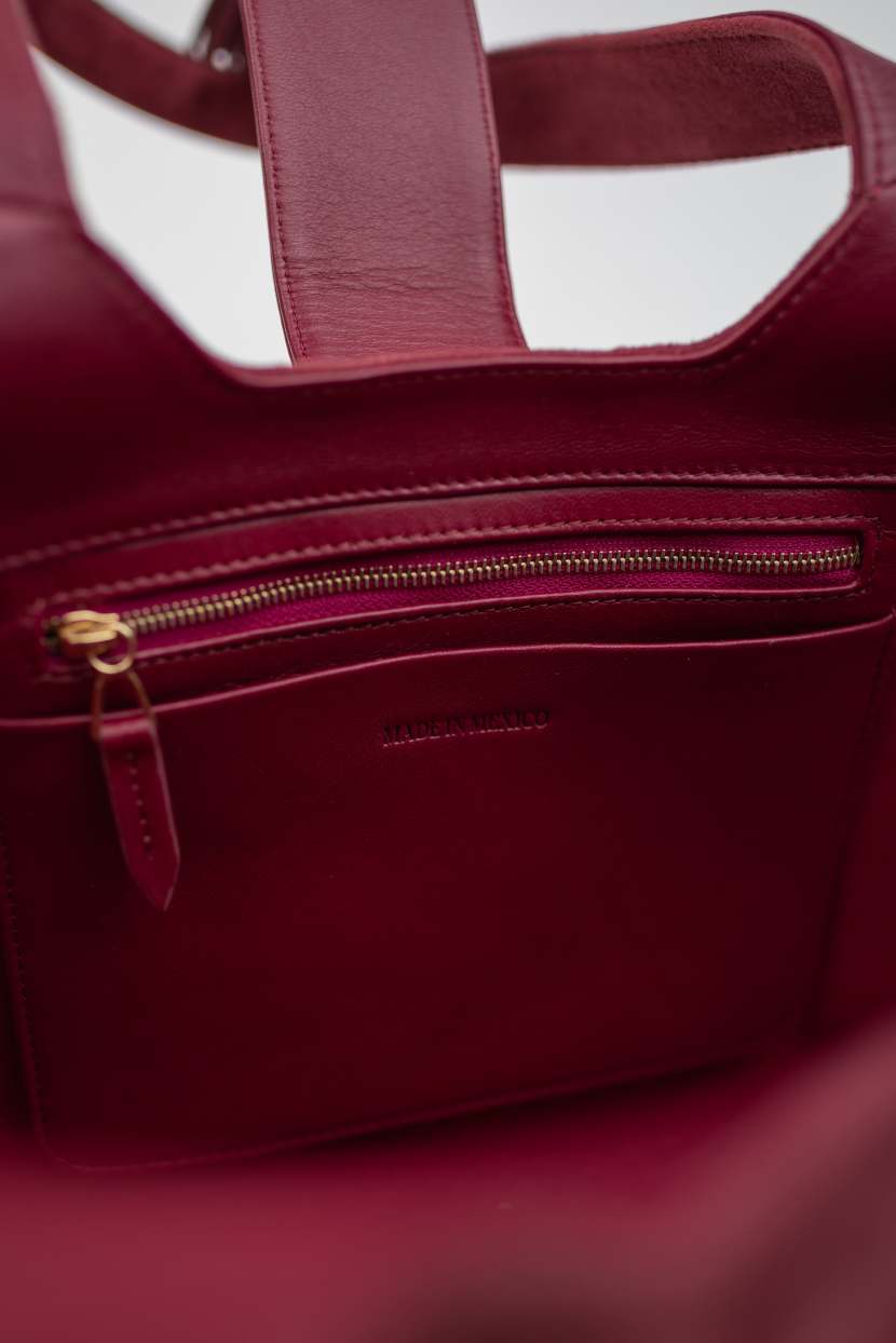 Close-up of a burgundy leather tote bag showing the interior pocket with a gold zipper and the debossed brand name 'LAURA RIVERA'.