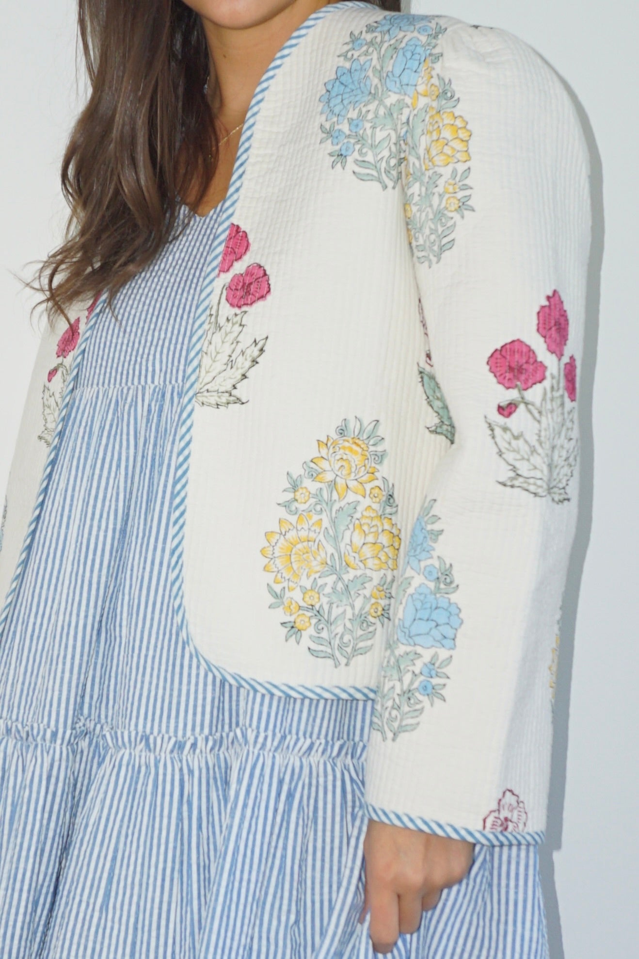 Person wearing a blue striped dress with floral embroidery on a plain background