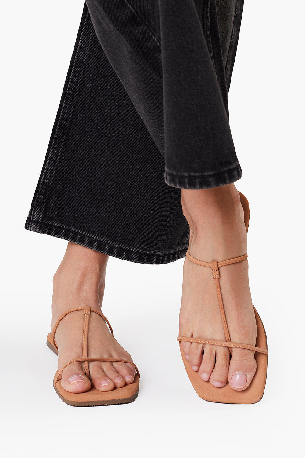 Tan sandals worn with black pants on a white background