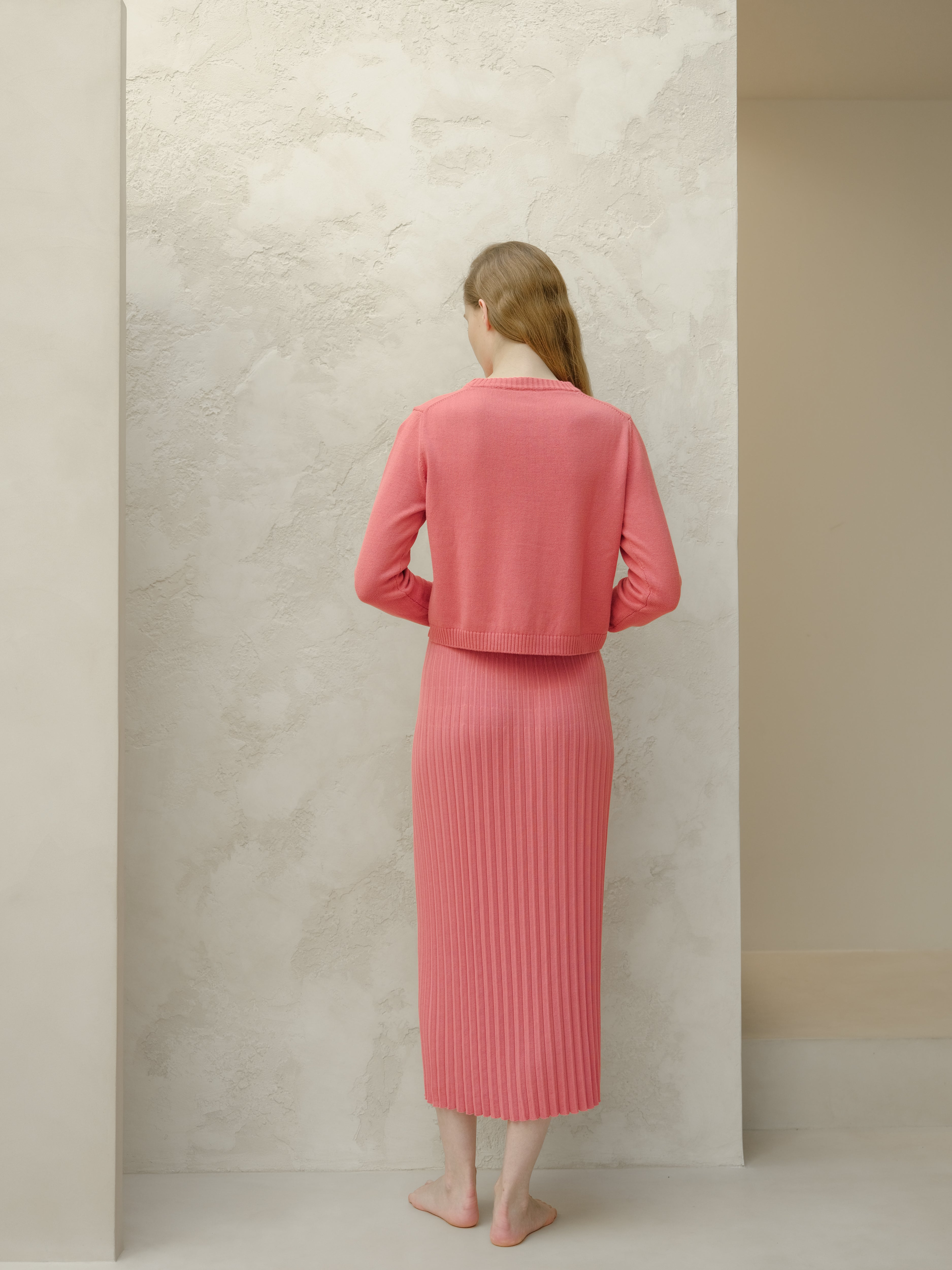 Woman wearing a pink outfit standing against a neutral wall.
