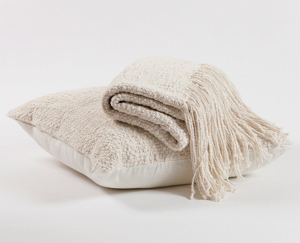 Folded beige blanket with tassels on a pillow against a white background