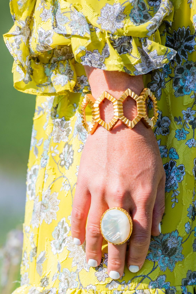 Hand wearing gold rings with a yellow floral dress in the background