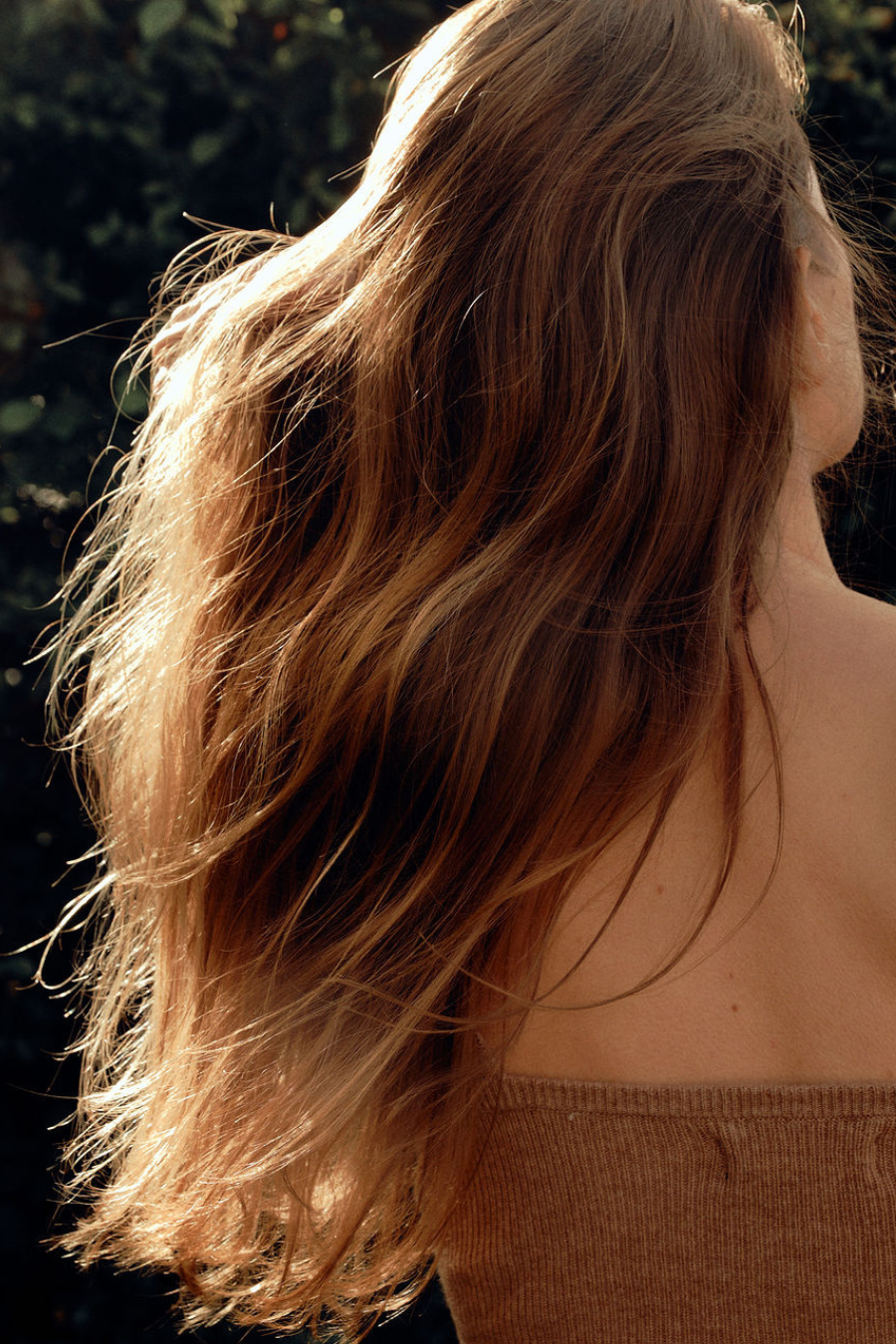 Close-up of a person with wavy hair wearing a brown top against a blurred natural background