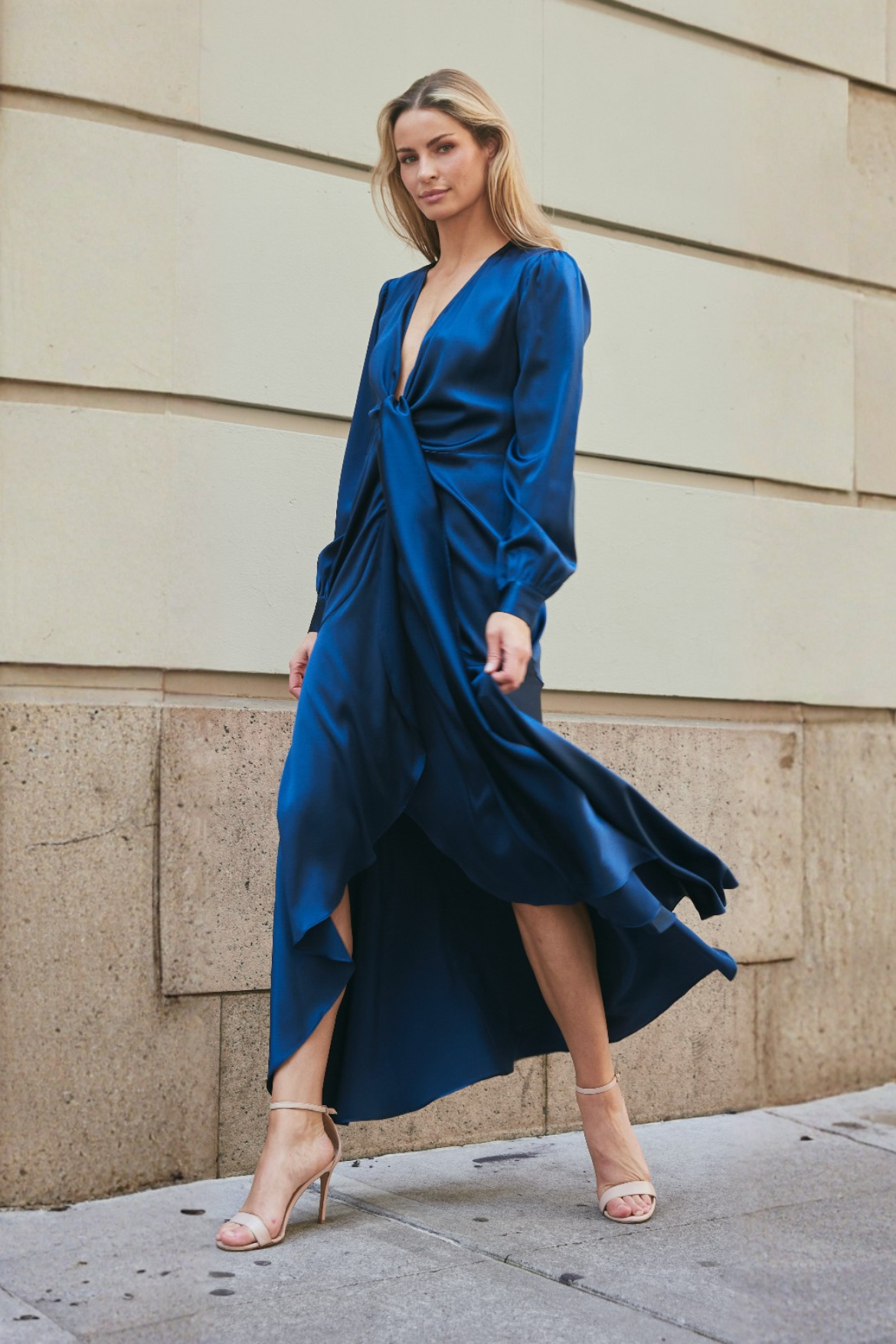 Woman in a blue dress standing against a beige wall.