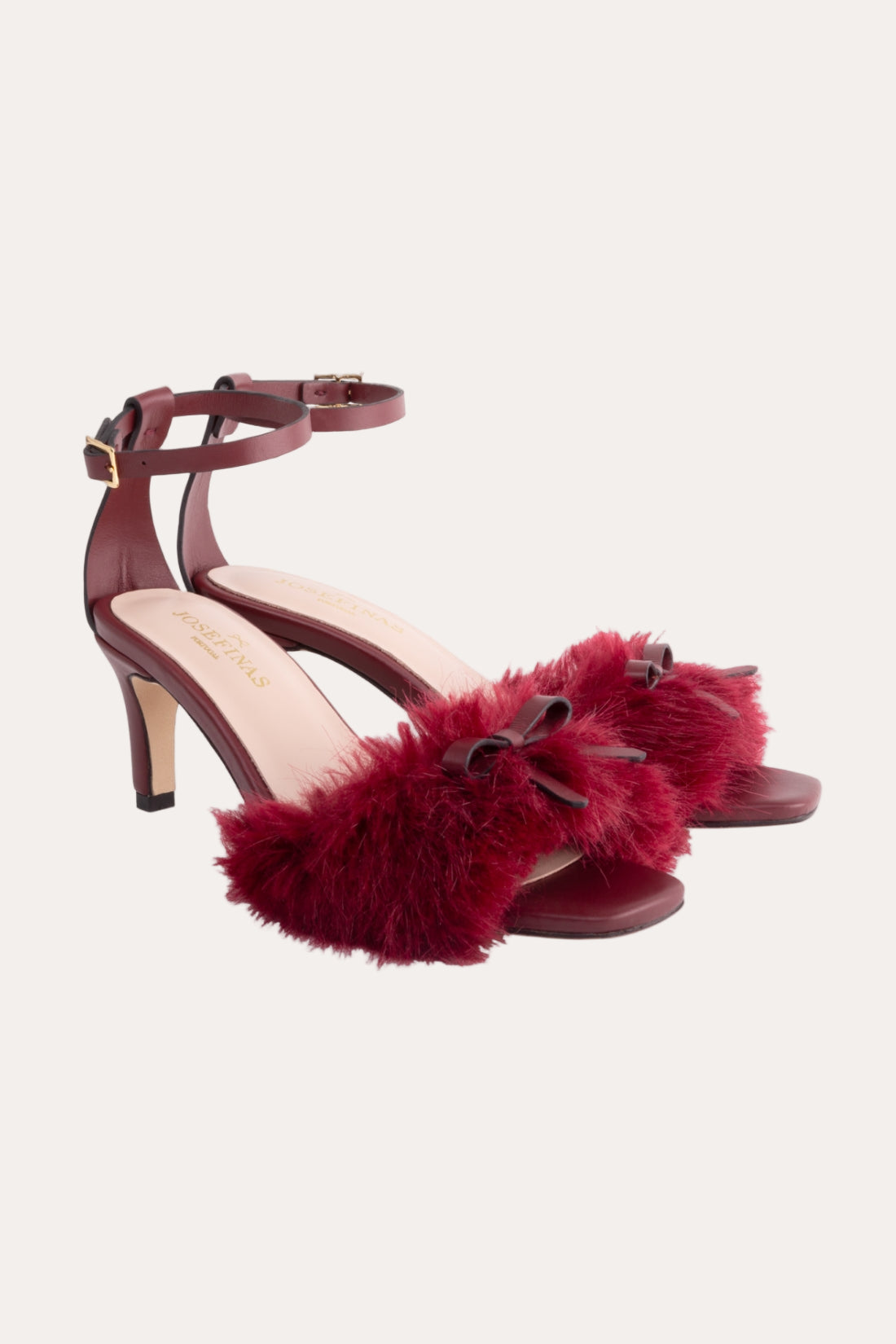 Red high-heeled sandals with fur details on a white background