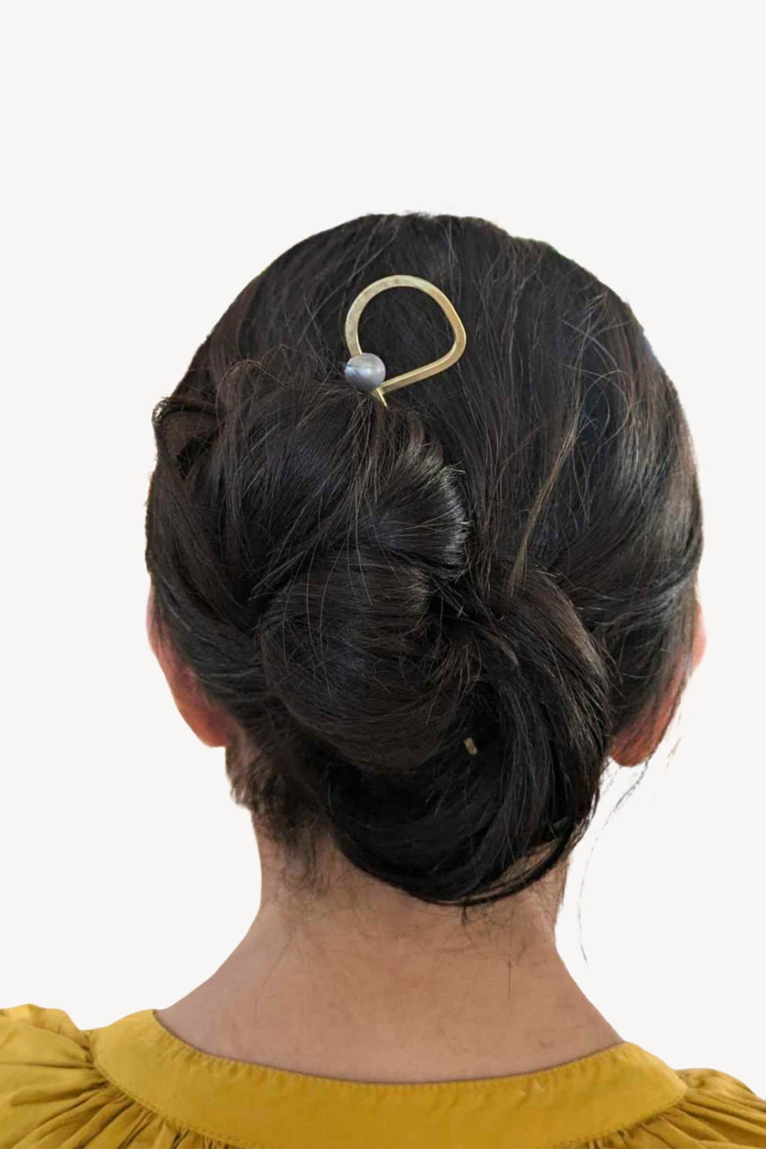 Person with a bun hairstyle featuring an abstract gold hair pin with a pearl