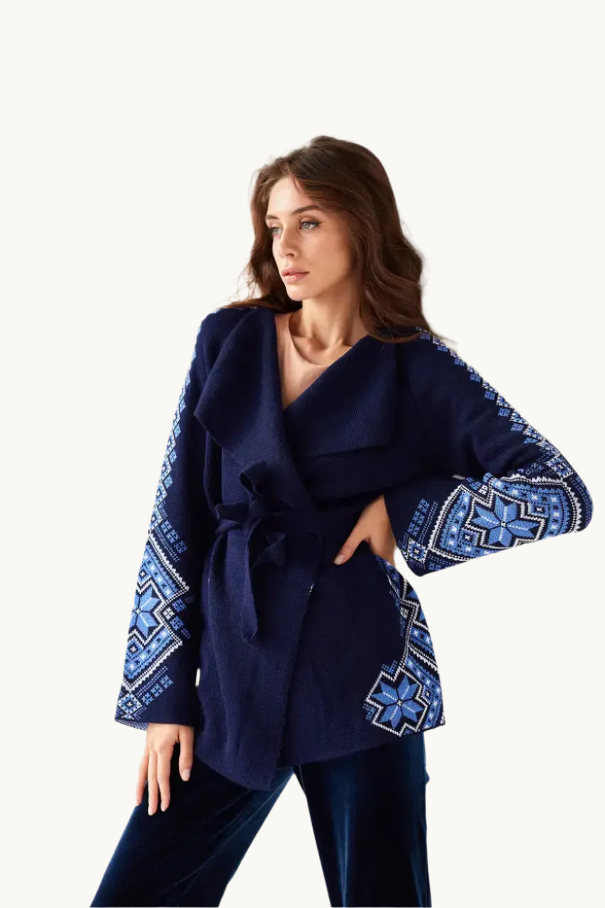A woman wearing a deep blue knitted cardigan with geometric patterns on the sleeves, paired with dark pants.