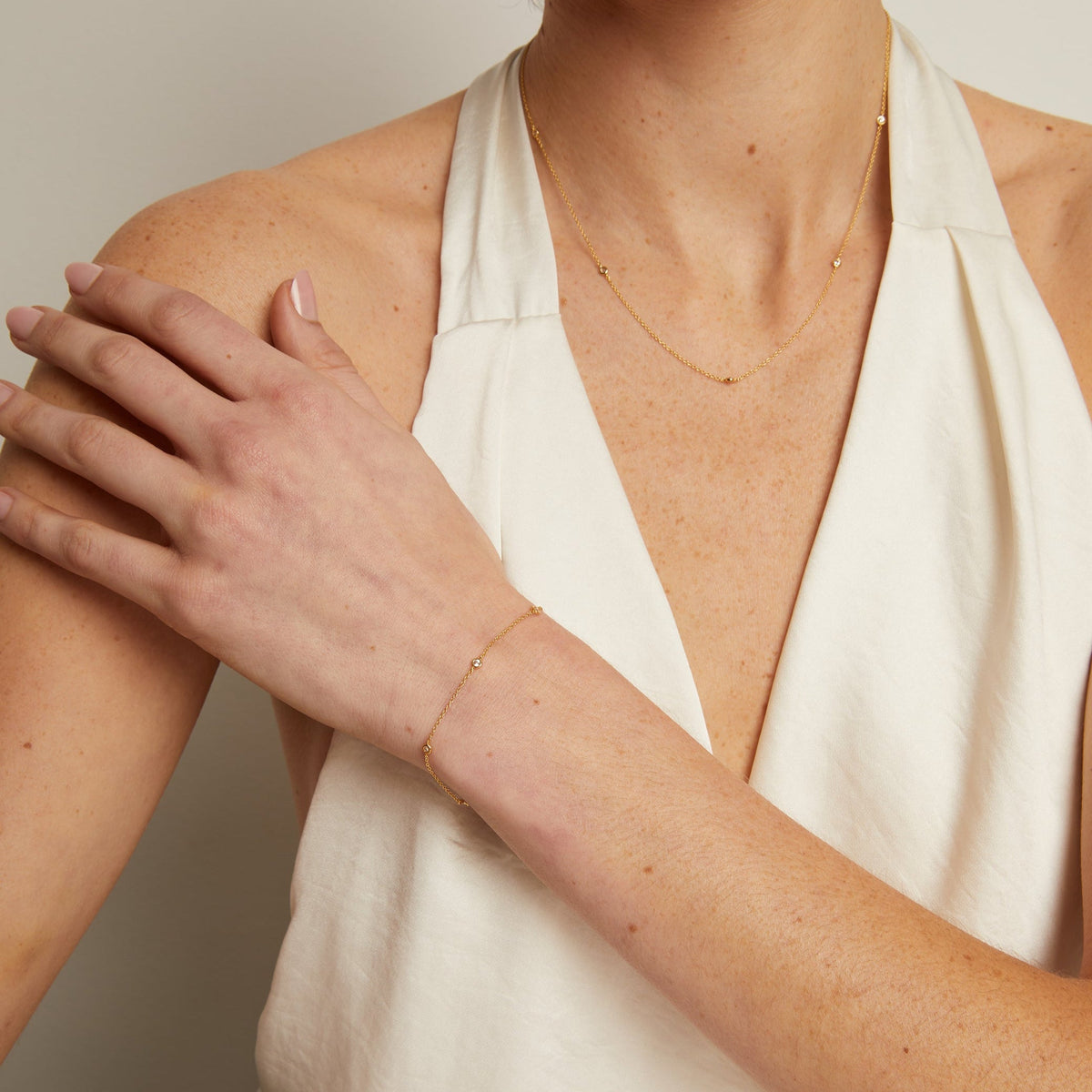 Person wearing a gold necklace and bracelet on a neutral background