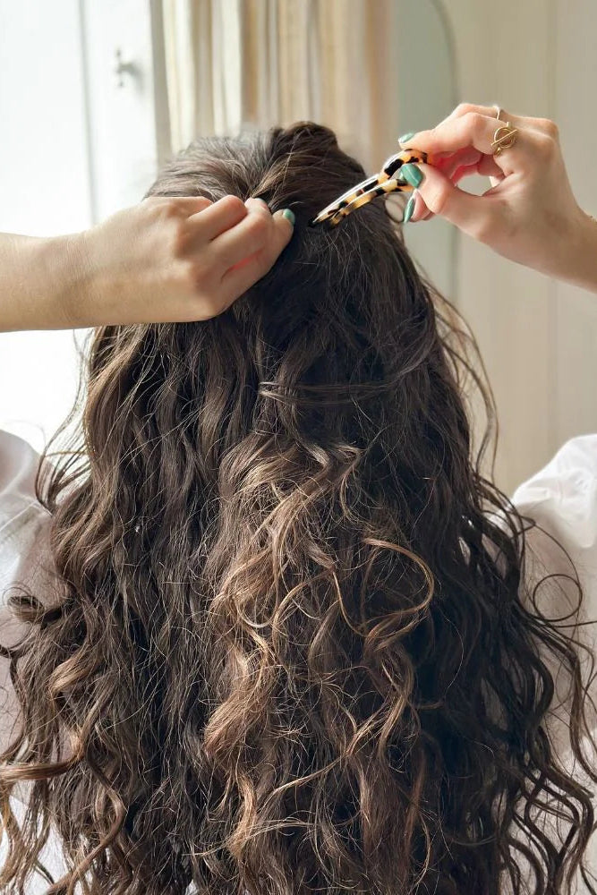 Person styling another person's hair with a clip in a bright room.