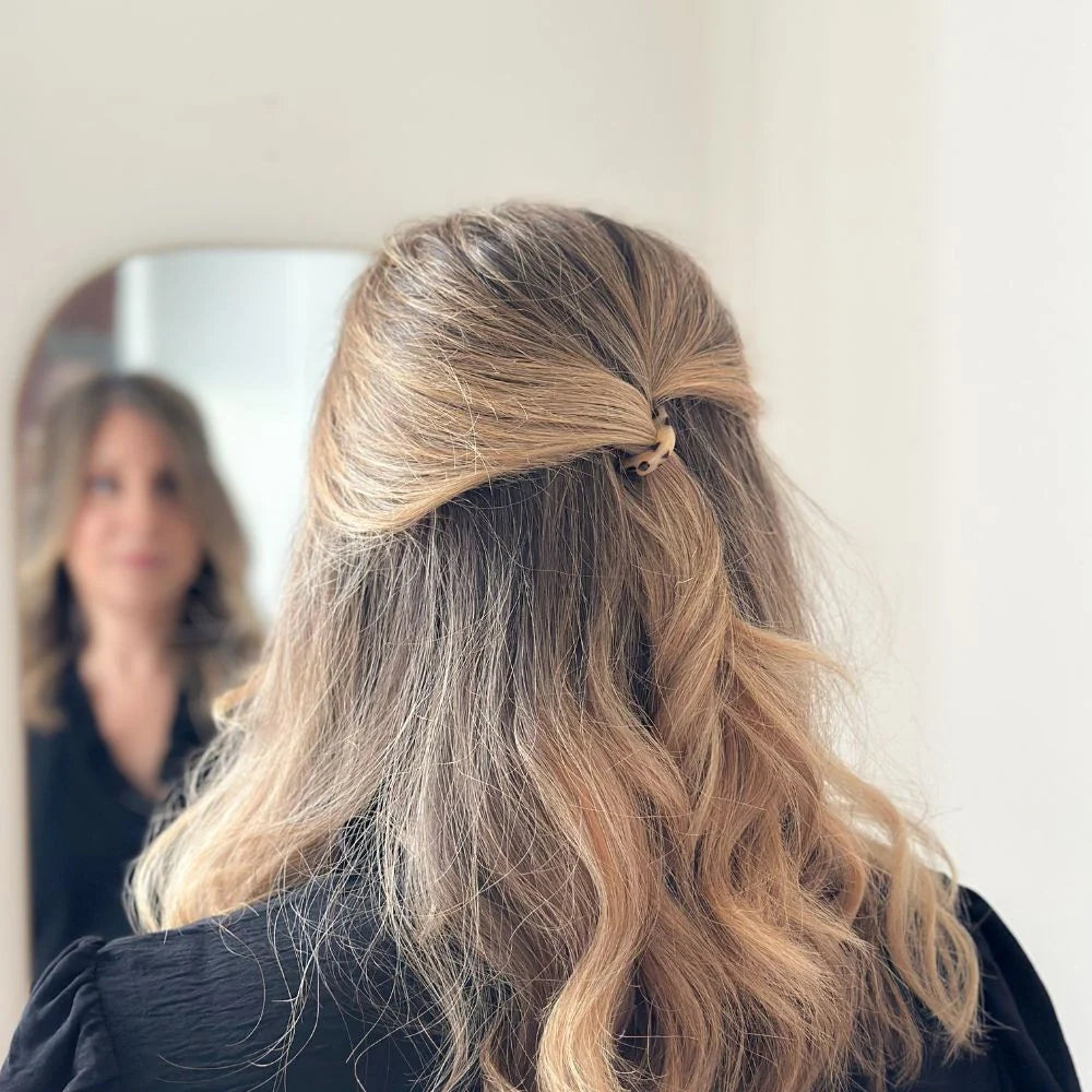Person with wavy blonde hair styled with a hair tie, looking into a mirror.