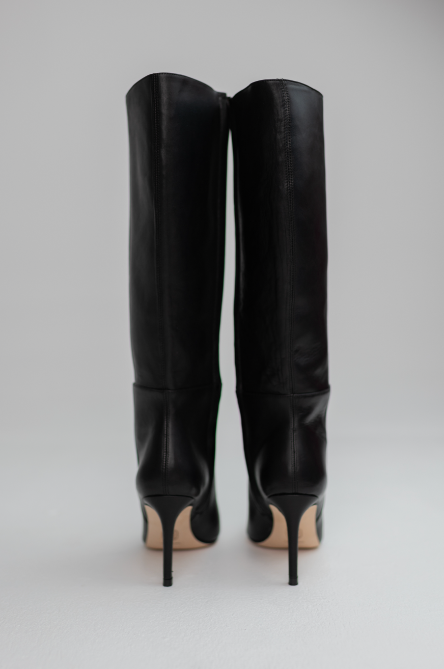 A pair of black leather knee-high stiletto boots shown from the back against a light gray studio background.