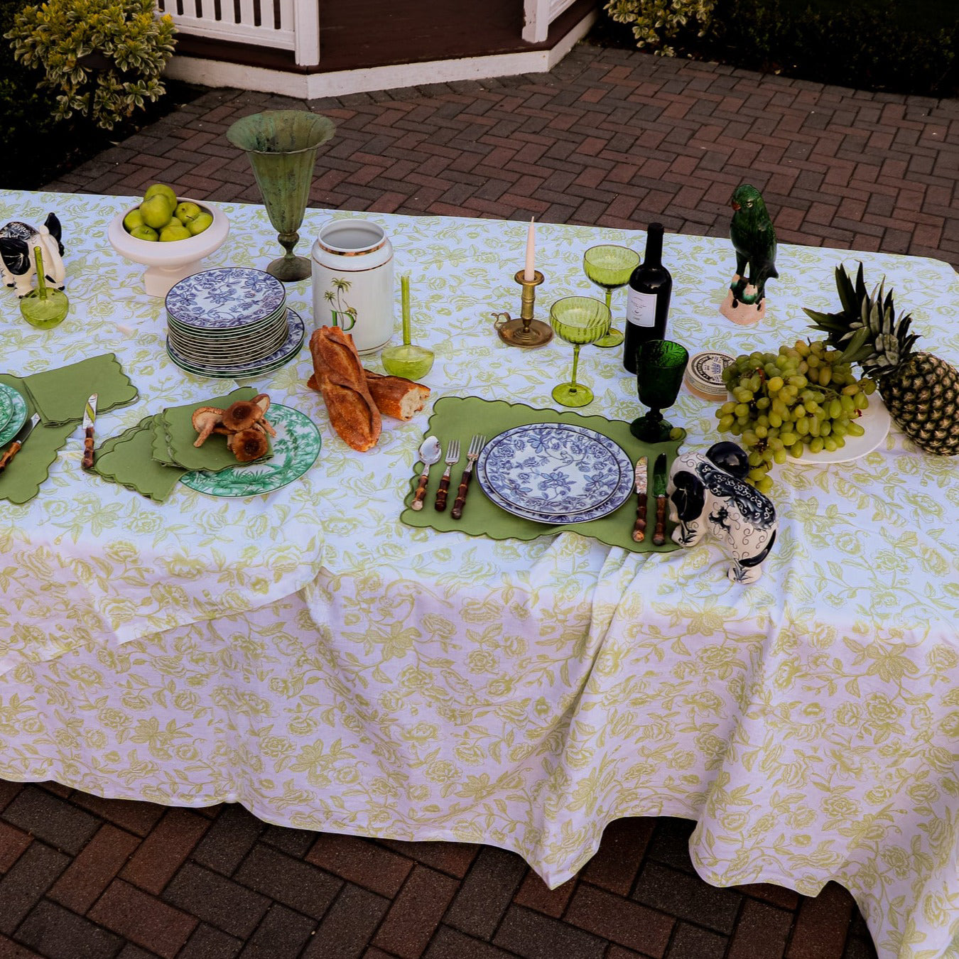 Decorated outdoor table with food, drinks, and tableware on a patterned tablecloth.