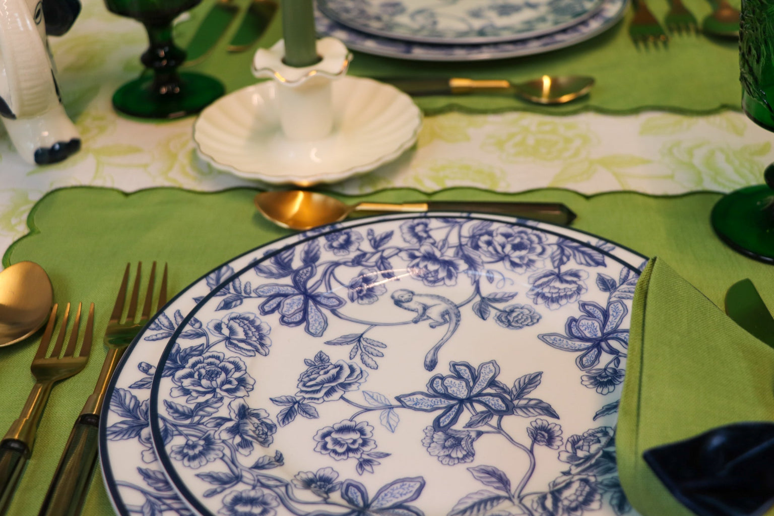 Dining table setting with blue floral-patterned plates, silverware, and a green tablecloth.
