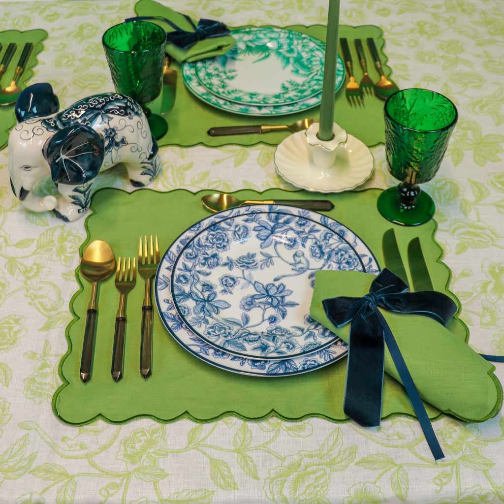 Decorative table setting with green placemats, blue and white plates, and green glasses on a floral tablecloth.