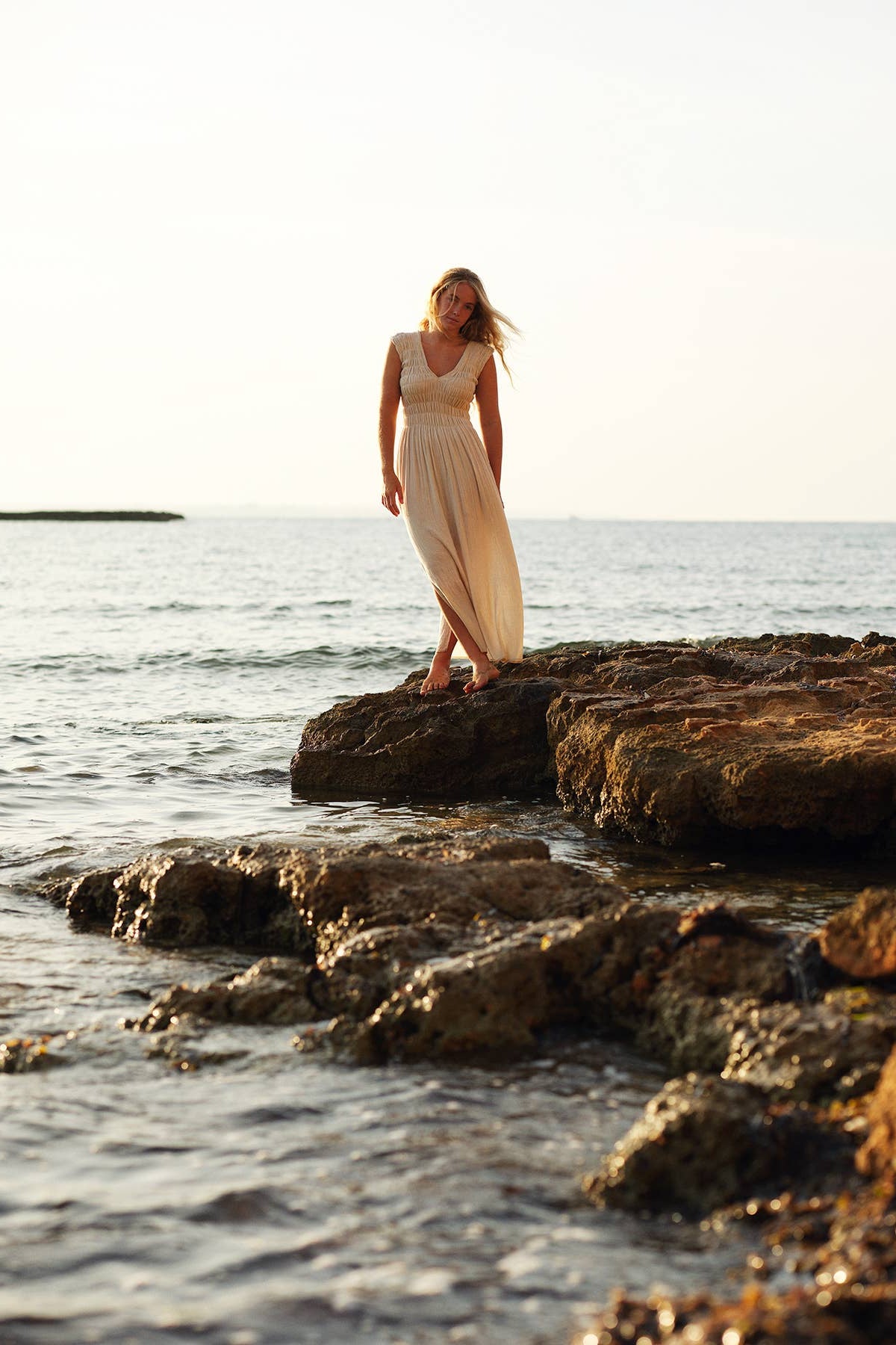 Woman in a long dress standing on rocks by the ocean