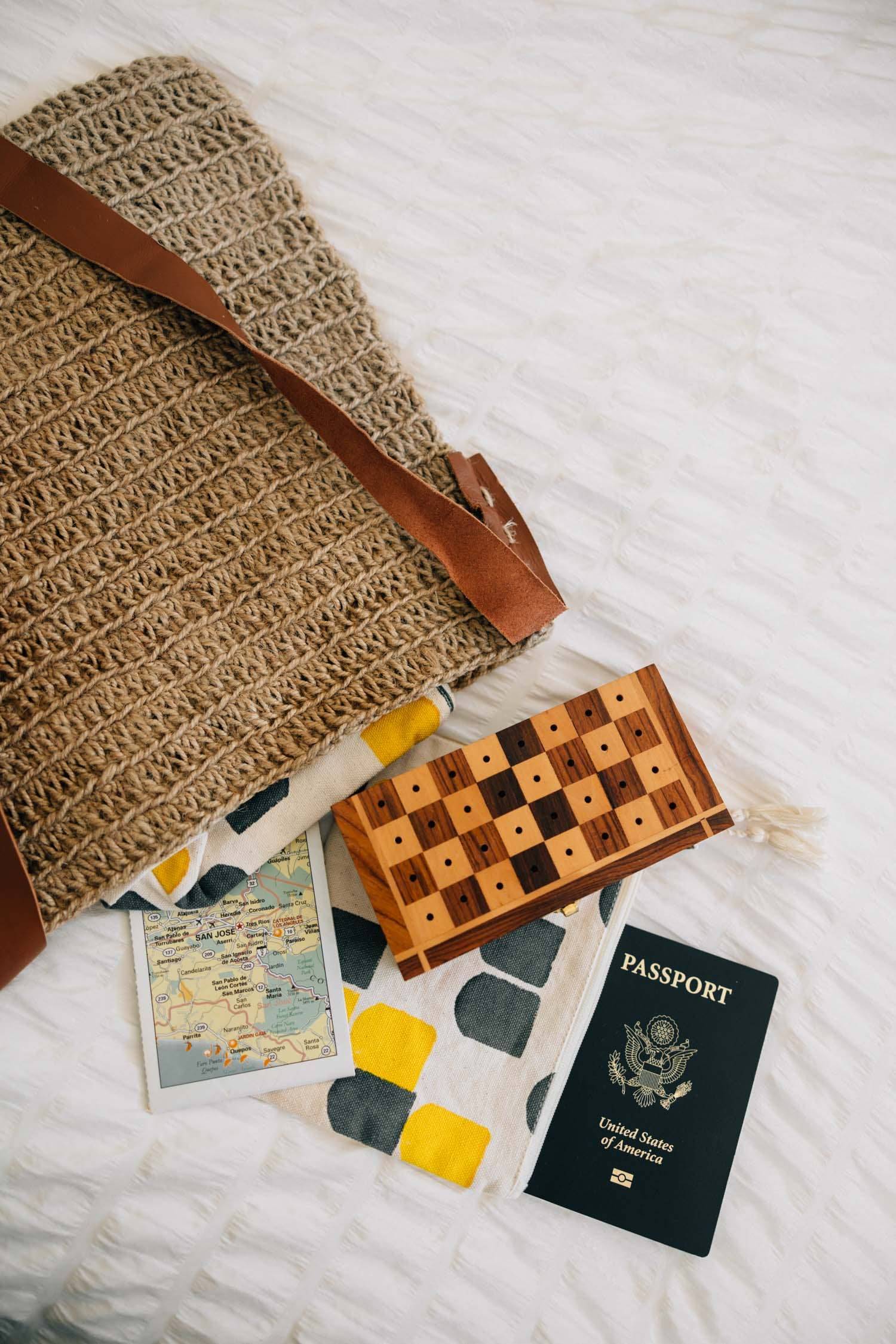 Wooden checkers board, travel map, and passport on a white surface