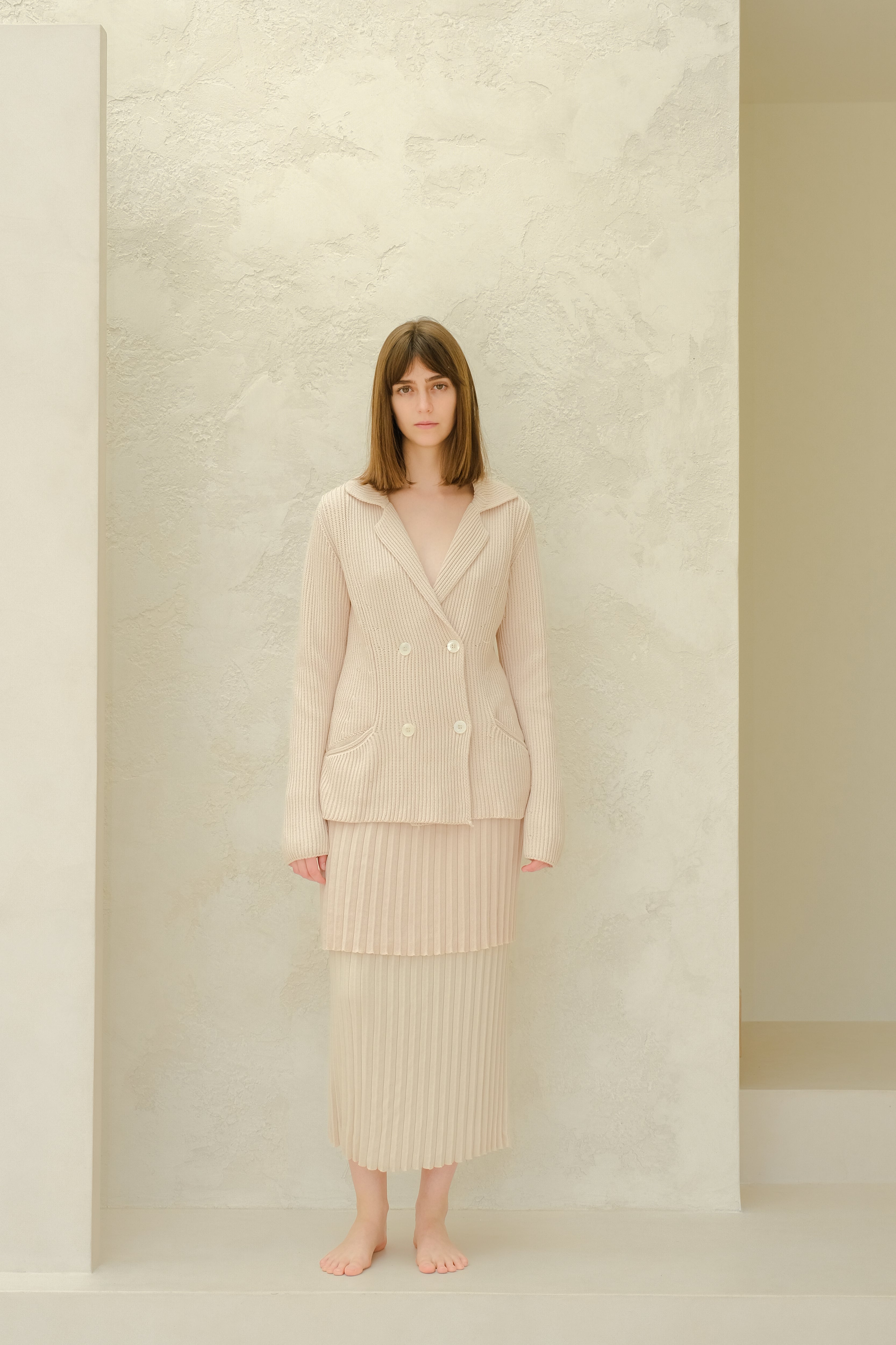 Woman wearing a light pink outfit standing against a neutral background