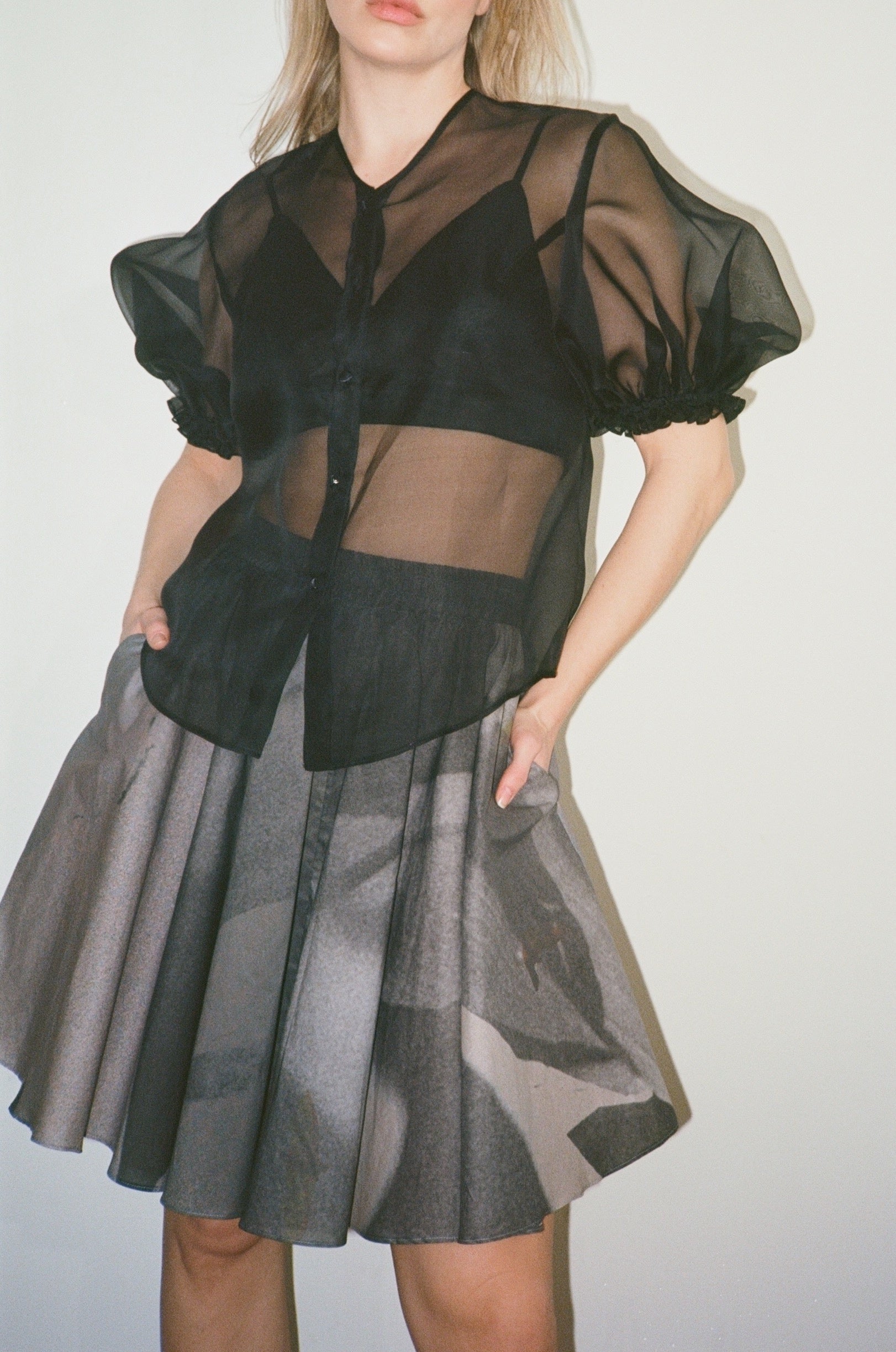 Person wearing a black sheer top and gray skirt on a white background