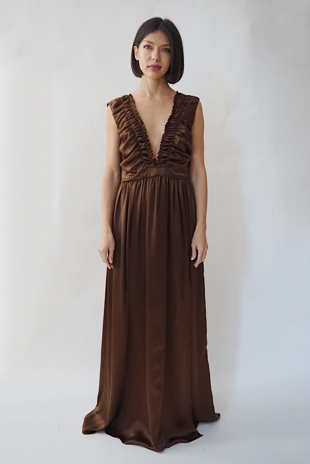 Woman wearing a brown silk gown with a ruffle neckline against a white background