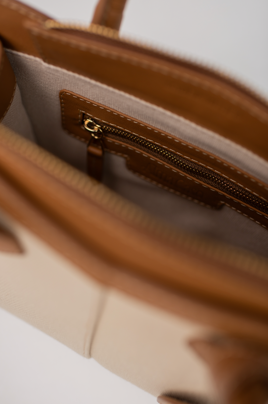 Close-up of the interior of a tote bag showing a tan leather interior pocket with a gold zipper and a beige fabric lining.